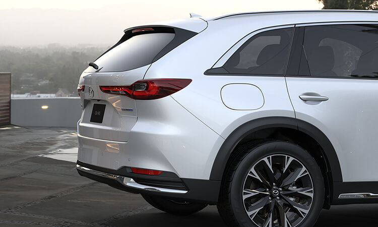 Artisan Red CX-90 almost straight grille on, making a turn in a city block.