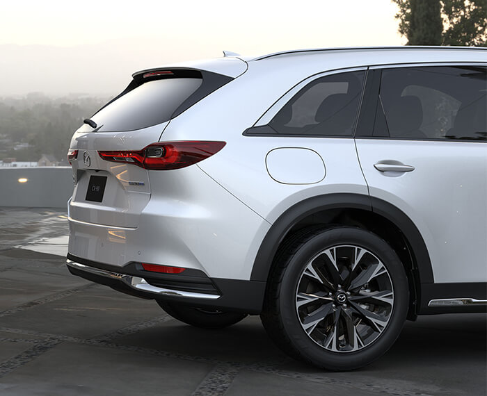 Artisan Red CX-90 almost straight grille on, making a turn in a city block.
